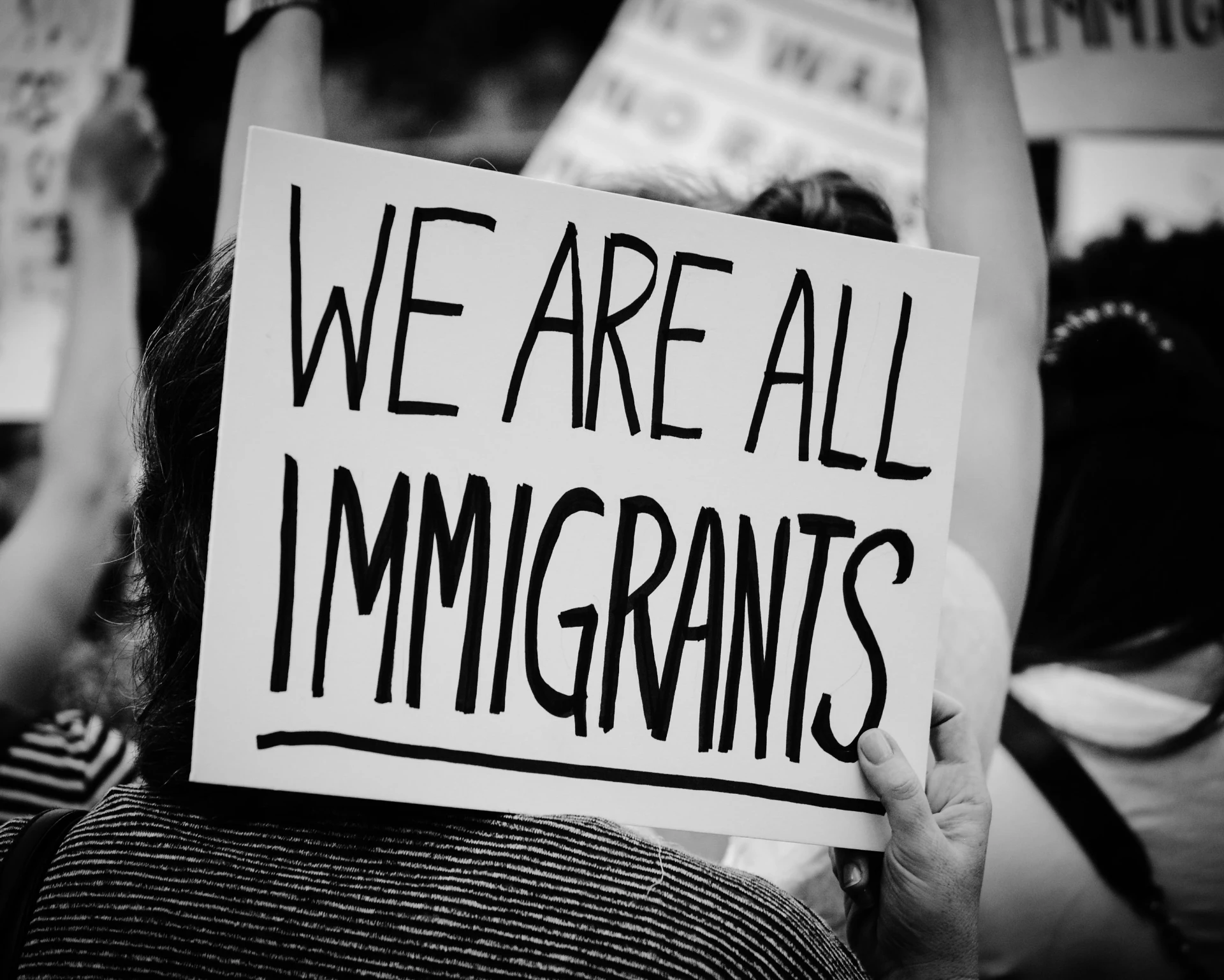 A marcher holding a hand-painted sign reading 'We Are All Immigrants' above a crowd